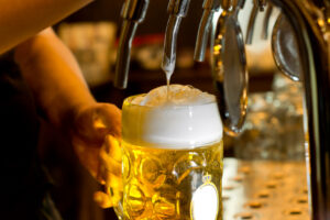 Close up of the hand of a man pouring a tankard of frothy draught beer from a stainless steel beer tap in a bar or pub into a large glass tankard